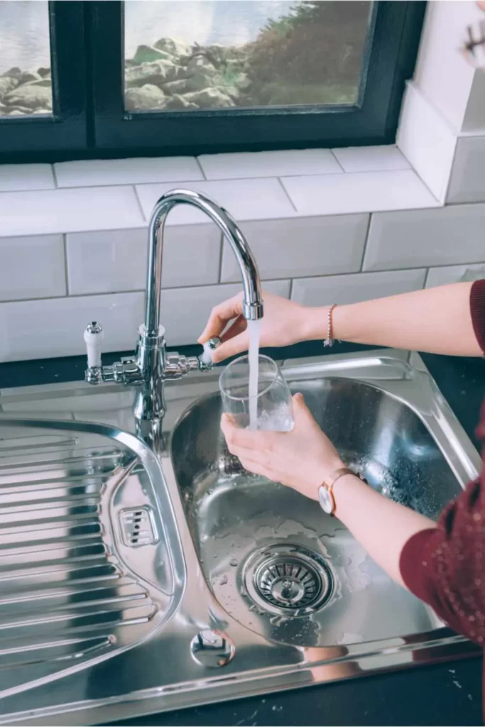 woman filling glass with water from steel faucet in kitchen